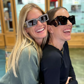 Two women smiling and wearing oversized designer sunglasses in a retail store